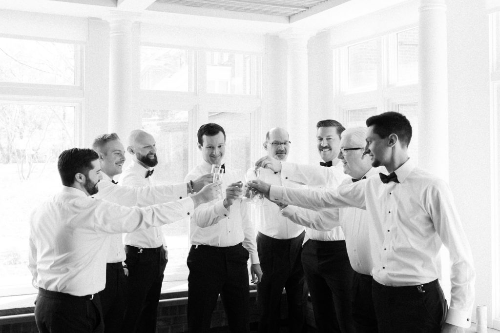 Black and white photo of groomsmen and dads doing a toast 