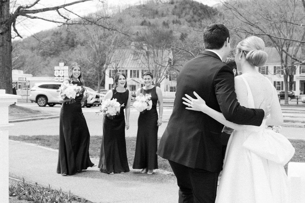 Bride and groom portrait for spring wedding at the Woodstock Inn in Vermont with bridesmaids looking on 