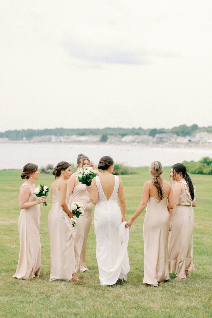 Candid photo of bride and bridesmaids taking photos on the coast of New Hampshire