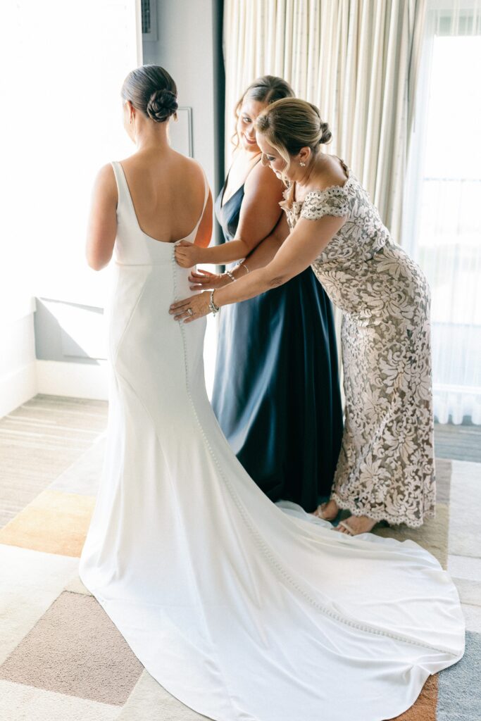 Bride getting into her wedding gown with the help of her mom and maid of honor of Newport wedding