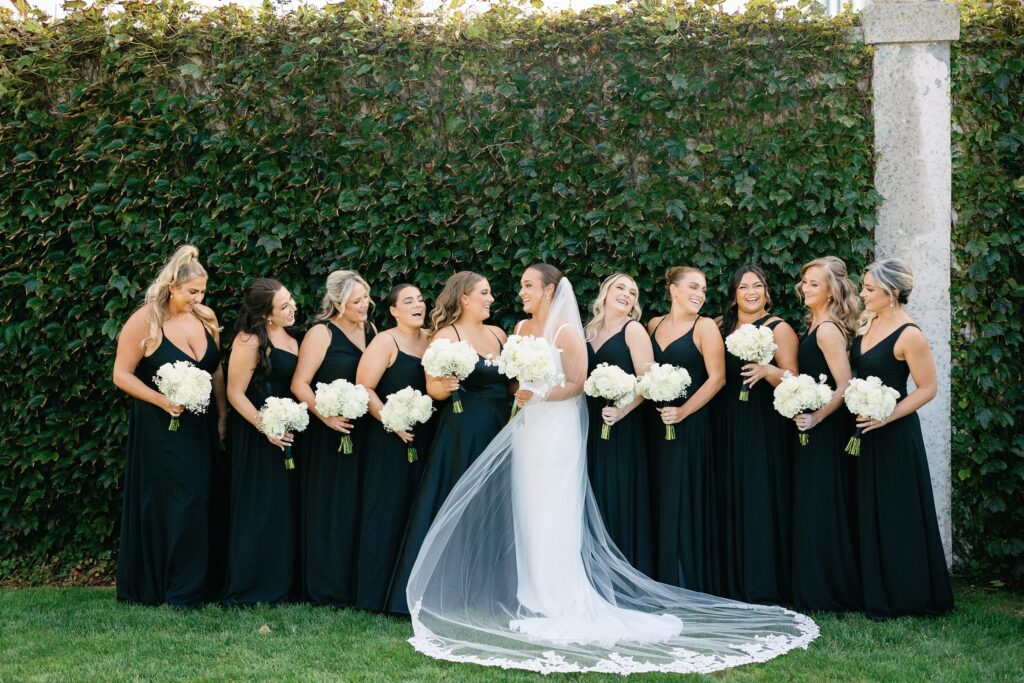 Bride and bridesmaids portrait for Belle Mer wedding in Newport, RI with bridesmaids wearing black dresses 