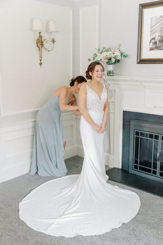 Bride putting on her wedding gown with the help of her bridesmaid for Boston city wedding