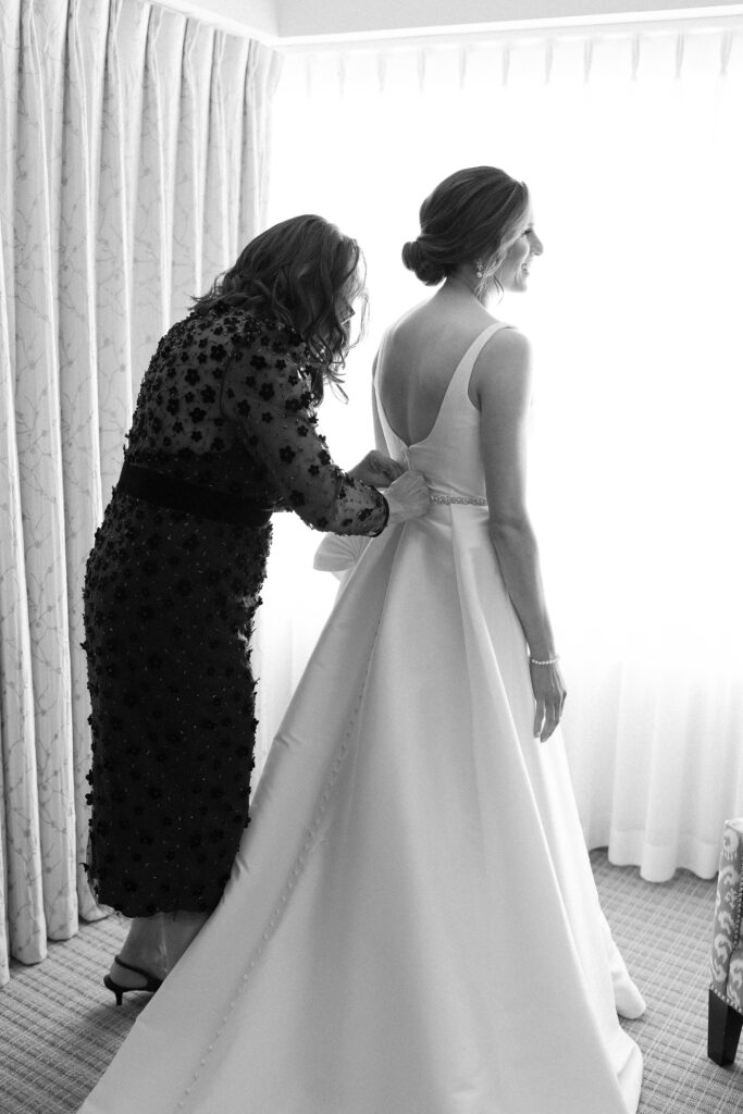 Black and white bridal portrait of bride putting on her gown
