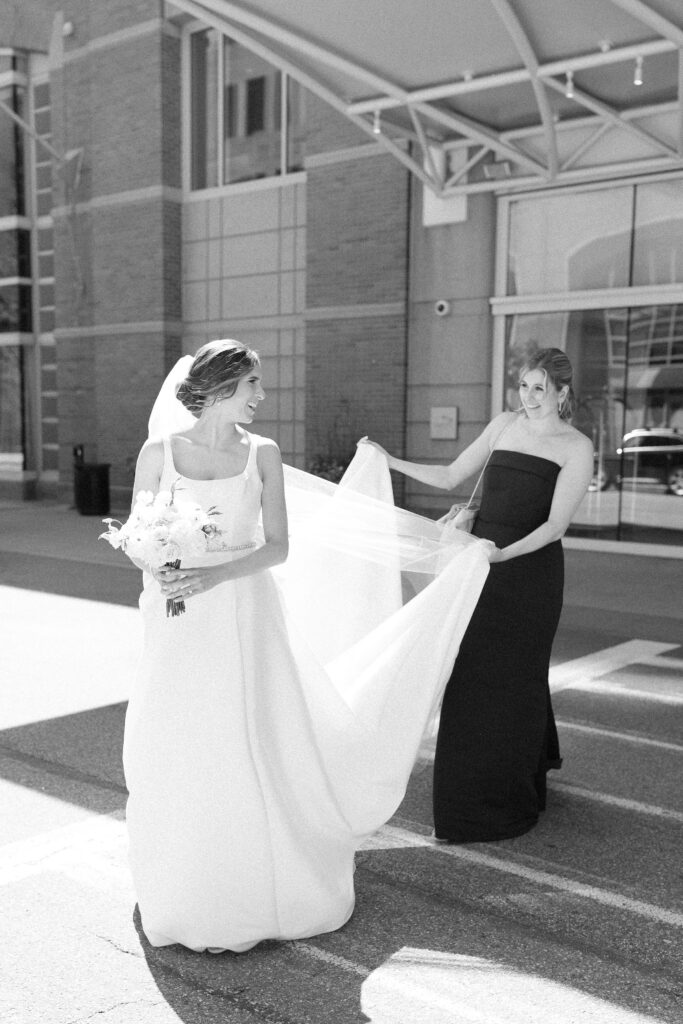 Bride with maid of honor holding veil while crossing this street for Boston wedding