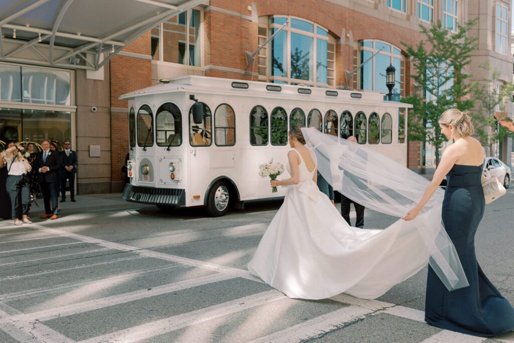 Bride crossing the street while maid of honor is holding her train in Boston