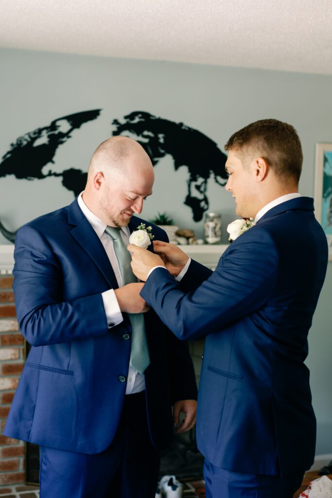 Groom putting on his boutonniere with the help of a groomsmen 