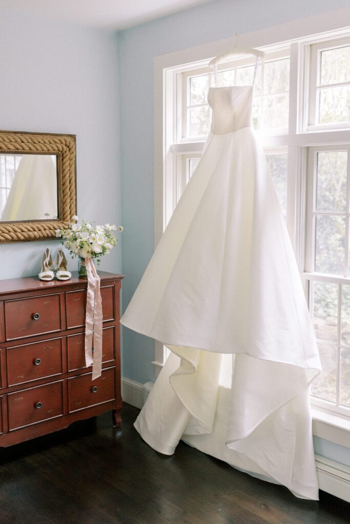 Bridal gown hanging in the window during getting ready portraits for Martha's Vineyard Tented wedding 