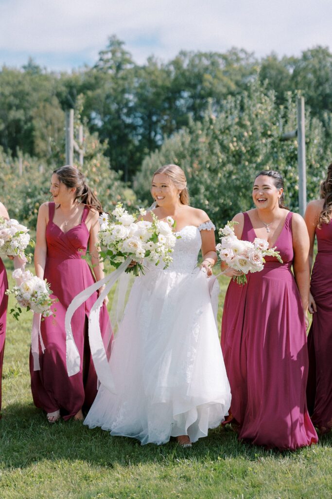 Bride and bridesmaids candid portrait in the orchard wearing mauve colored dresses 