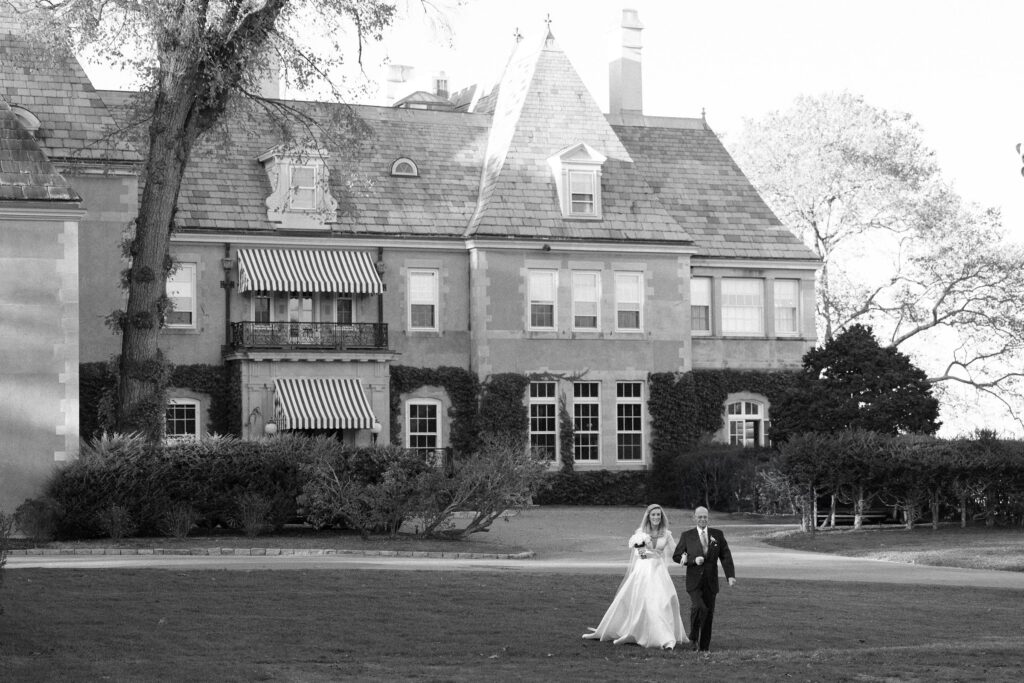Bride walking across the lawn into the ceremony with her father at New York Yacht Club Harbour Court in Newport